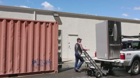 stainless refrigerator loaded in a pickup truck bed with a hand truck, face visible