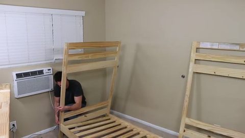 man kneeling to disassemble a bunk bed into two separate beds, face visible