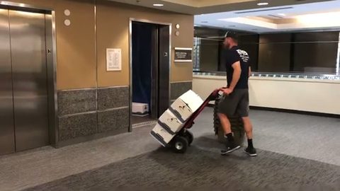 mover pushing a hand truck stacked with file boxes through an office lobby