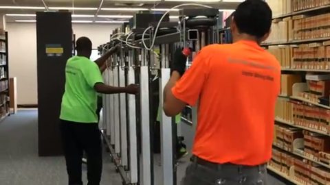 two movers relocating a fully loaded library shelving range on lift jacks