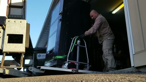 mover strapping a snack vending machine onto a hand truck at a truck liftgate, face visible
