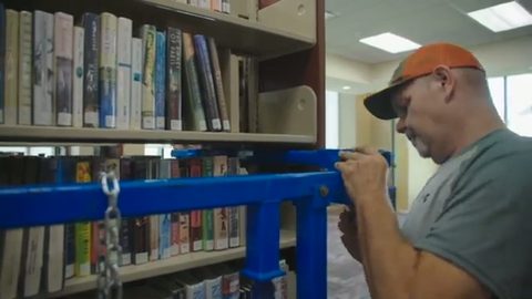 mover securing a loaded library shelving unit to a lift rig, face visible