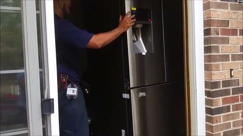 Mover guiding a stainless steel French-door refrigerator through a home doorway