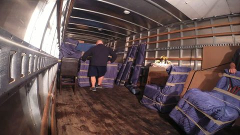 mover carrying a pad-wrapped item into a professionally loaded van-line moving trailer, back view